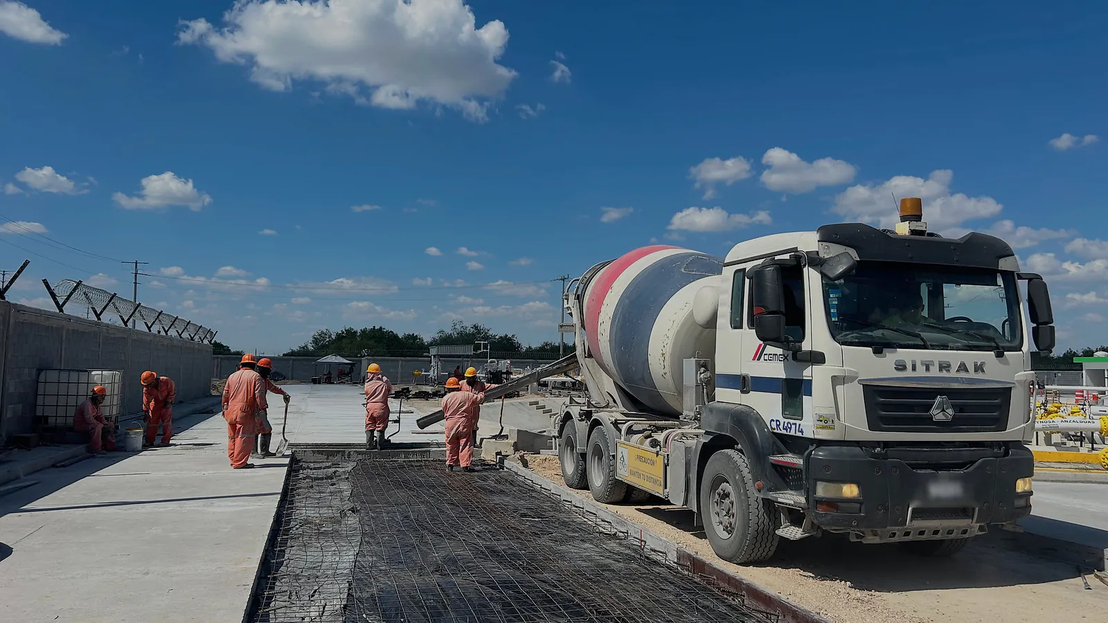 Una revolvedora descarga concreto por el canalón en el frente de colado de una vialidad, con la malla electrosoldada tendida en primer plano y la cuadrilla de overol naranja extendiéndolo, en la Estación Anzalduas